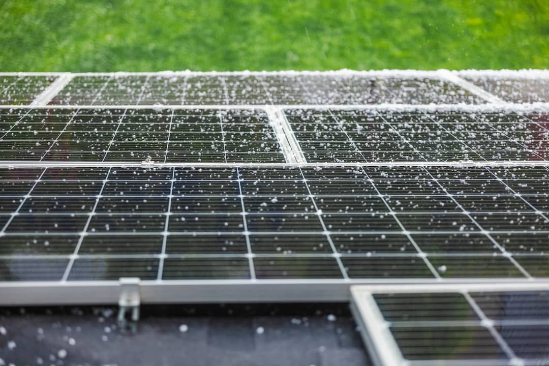 Solar panels on roof looking over green grass as rain and small hail stones land on them, answering question does hail damage solar panels?
